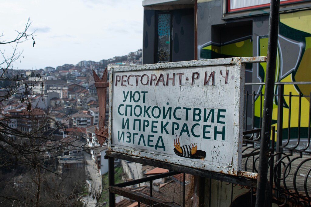 Старая вывеска ресторана с надписью «Уют, спокойствие и прекрасен изглед» на фоне городской застройки